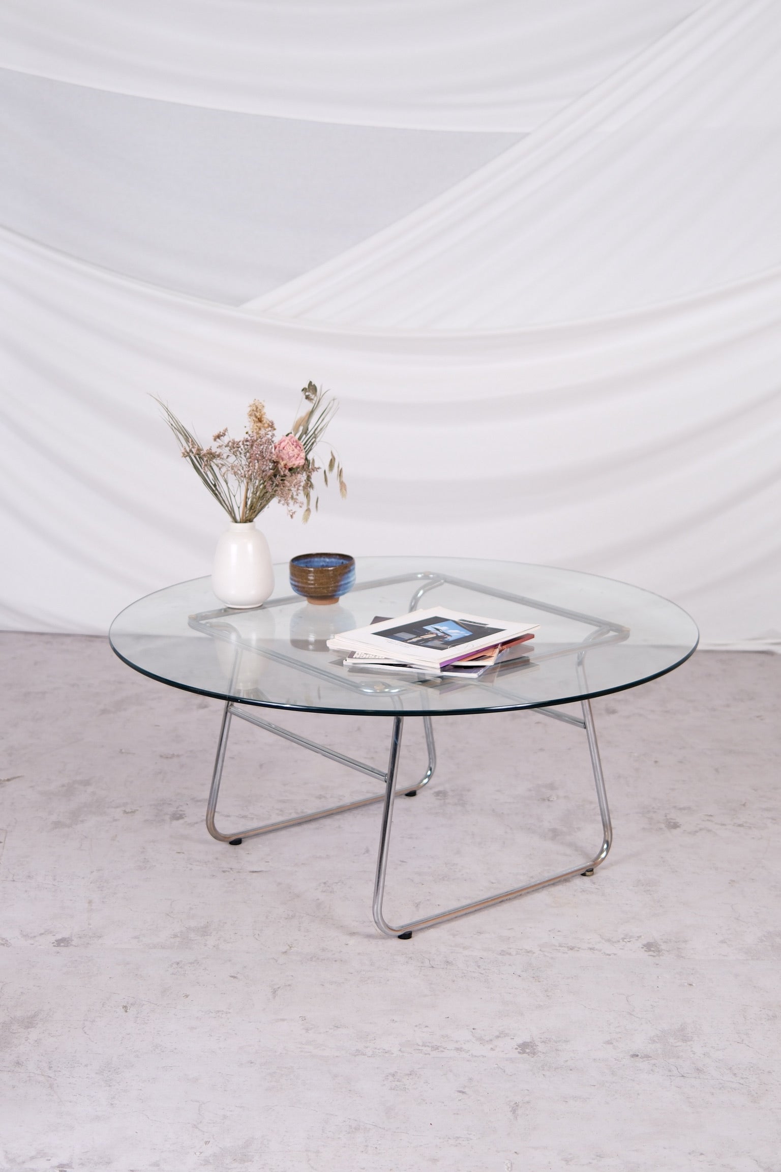 Glass coffee table with metal legs on a light gray floor against a white wall