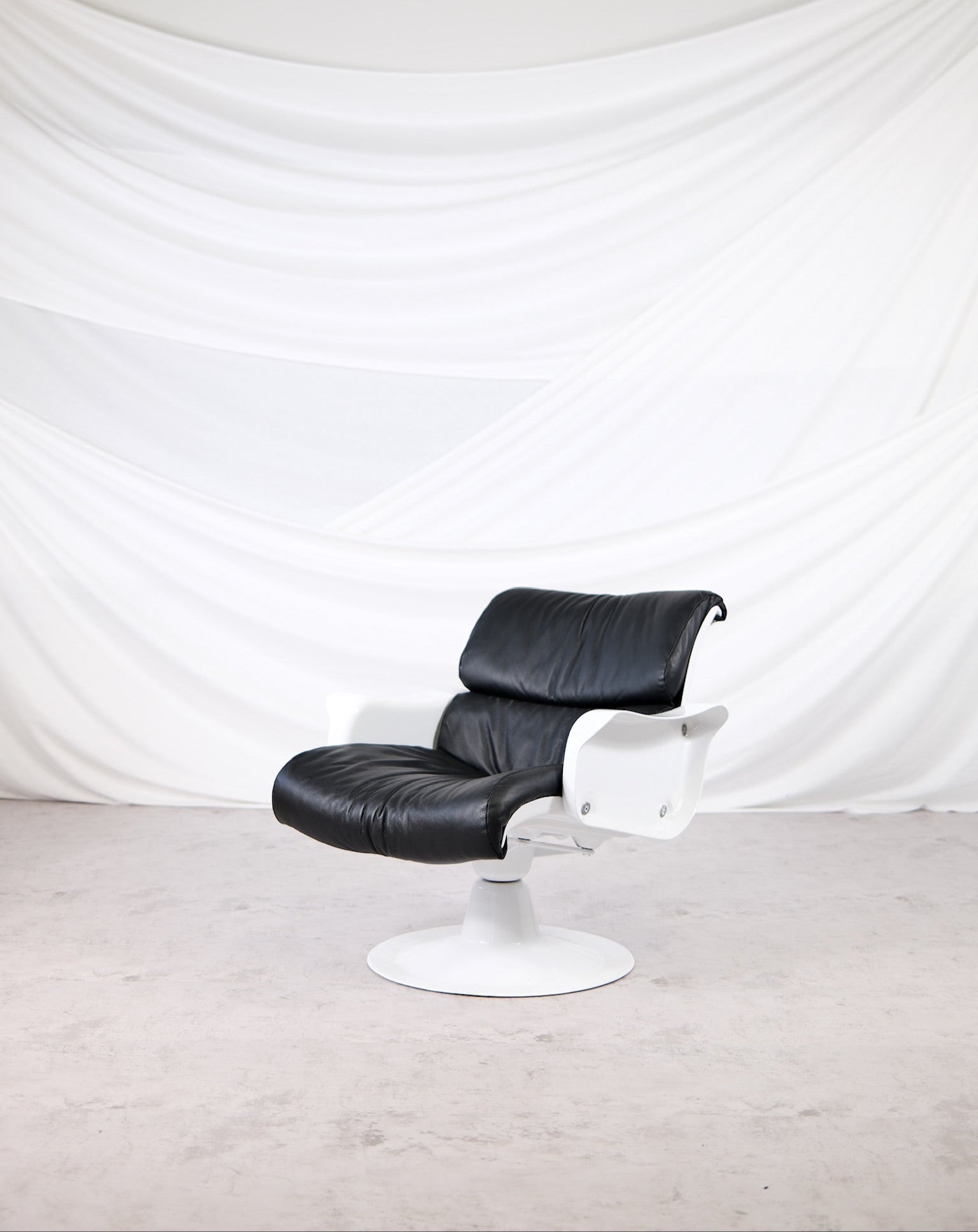 Yrjö Kukkapuro C-Saturnus lounge chair with white fiberglass frame and original black leather upholstery, photographed in a minimal studio setting.