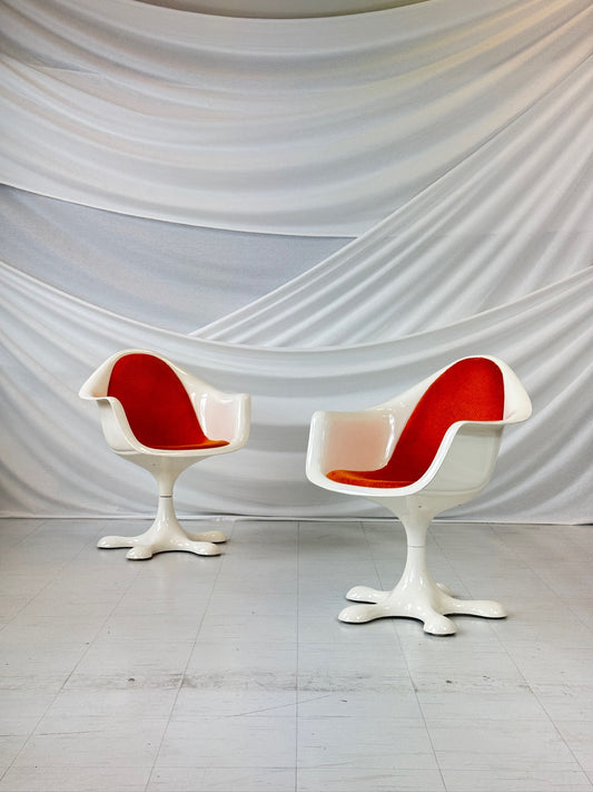 Set of five vintage Orion chairs by Eero Aarnio with white fiberglass frames and bright orange upholstery, featuring star-shaped swivel bases, arranged in front of a white draped backdrop.