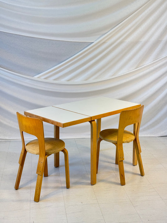 Vintage white Artek DL82 drop-leaf table with birch legs and white laminate top, styled with two Artek 66 chairs.