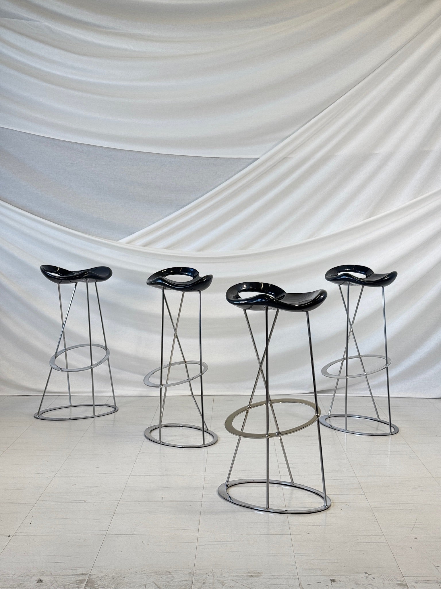 A group of four black glossy bar stools with organically shaped seats and chrome-plated steel legs, designed by Marco Maran for Rexite.