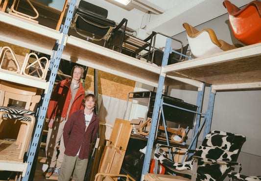 Two people among vintage chairs and furniture on storage shelves at Pino Interiors