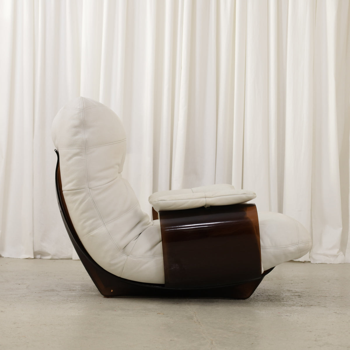 White lounge chair with dark curved side panel, profile