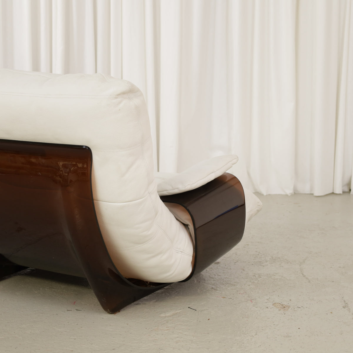 Detail of the sofa armrest, white upholstery and brown curved shell