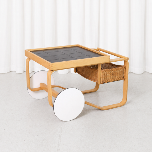 Vintage Artek 900 Tea Trolley designed by Alvar Aalto in 1937, featuring a bent birch frame, black ceramic tiles, rattan basket and white wheels.