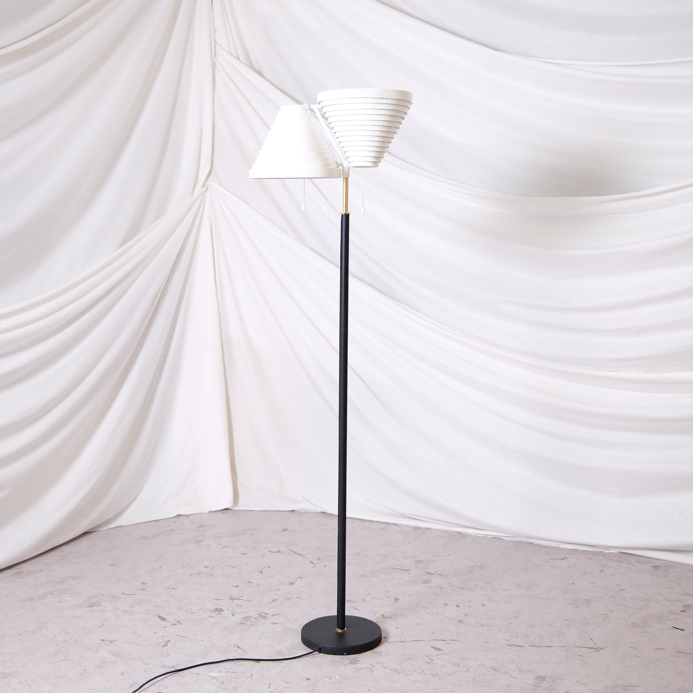 Vintage Artek A810 floor lamp by Alvar Aalto with white layered shades, black stem and brass details. Finnish design lighting from Helsinki, worldwide shipping available.