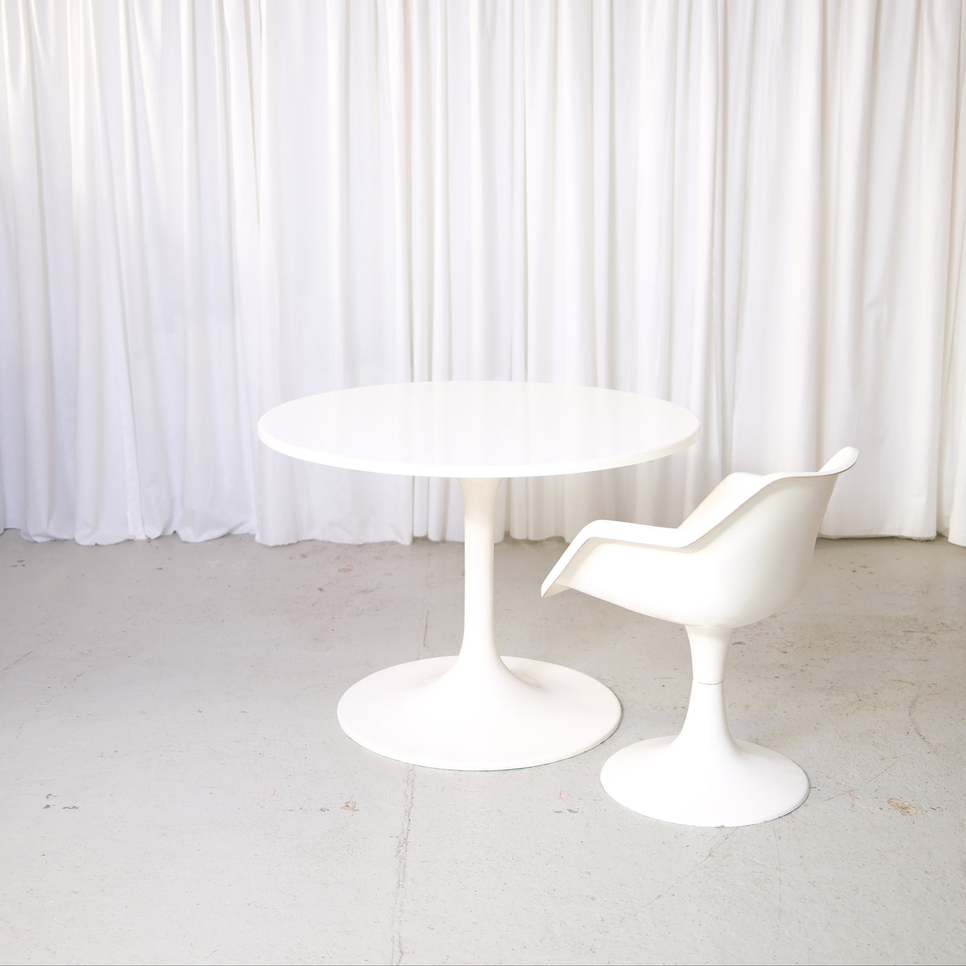 Vintage Asko Amigo round white dining table with pedestal base in front of white curtains.
