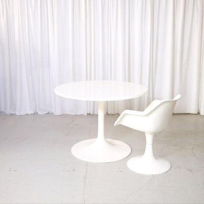 Vintage Asko Amigo round white dining table with pedestal base in front of white curtains.