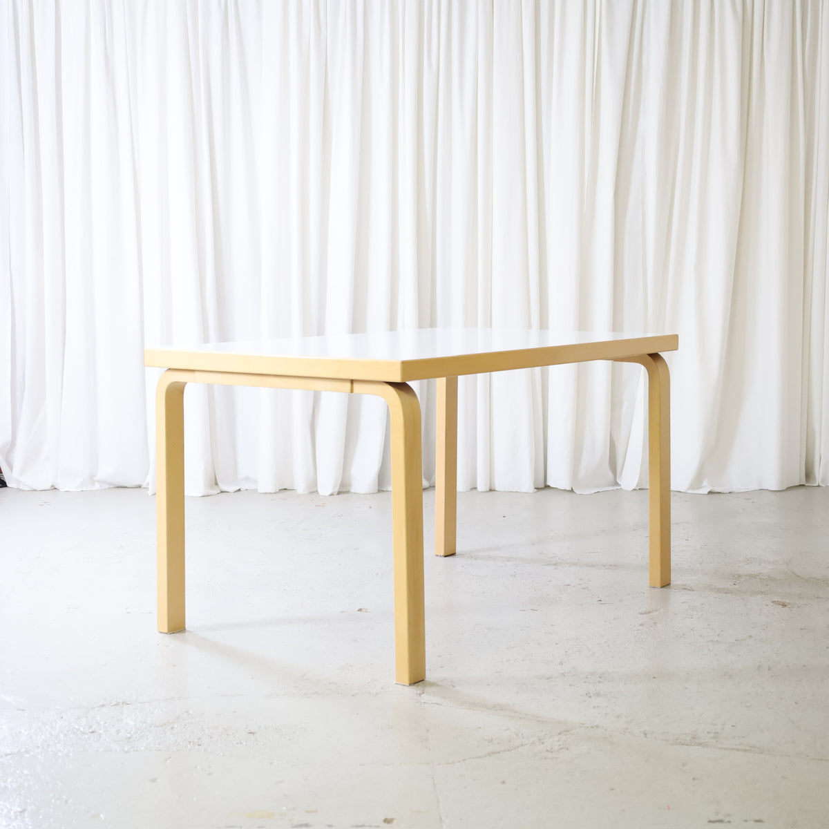 Alvar Aalto dining table by Artek with white laminate top and birch frame, angled view