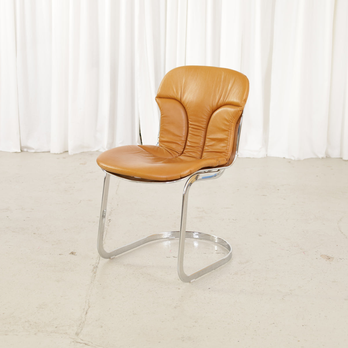 Cidue dining chairs in cognac leather with polished chrome cantilever frames and detailed padded backs