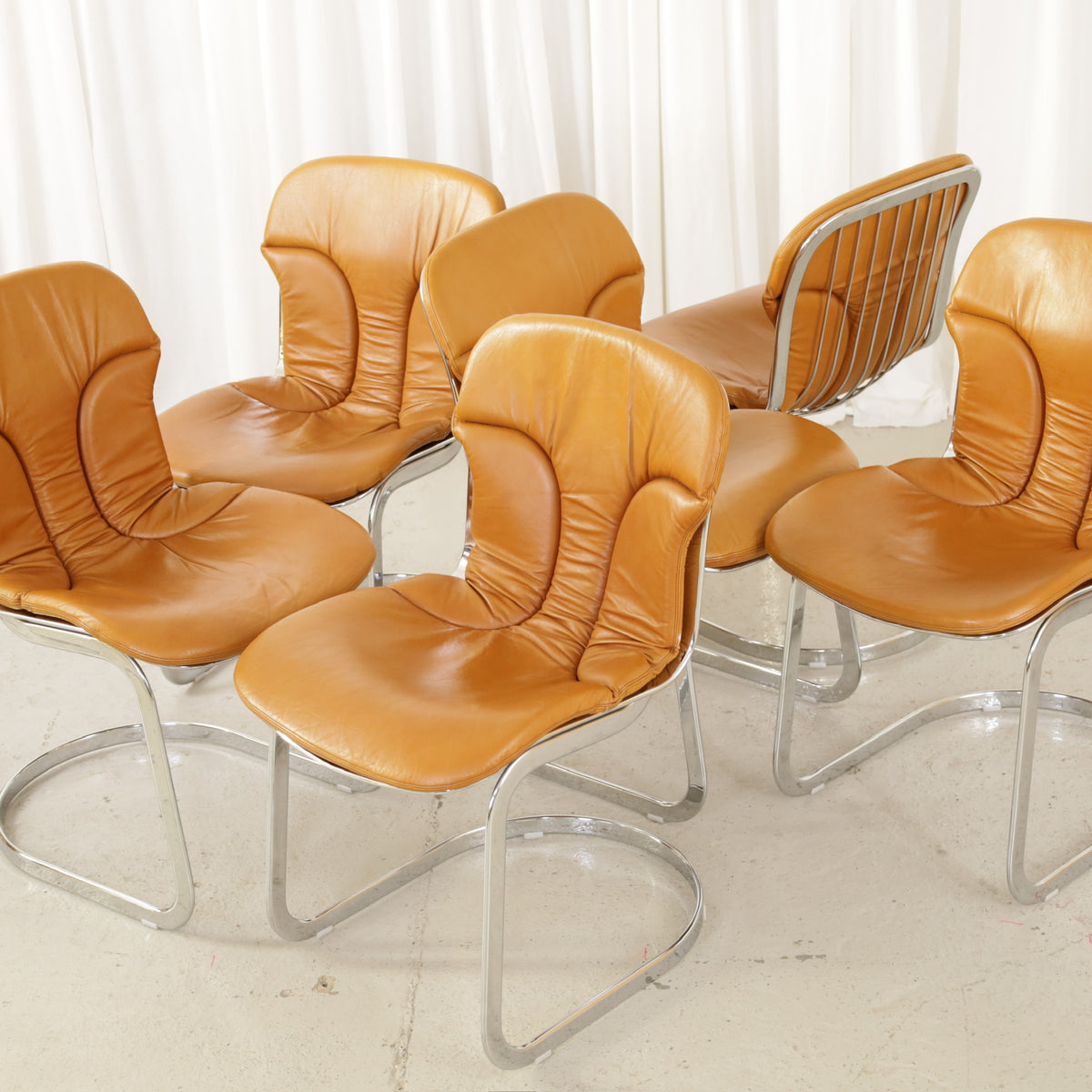 Cidue dining chairs in cognac leather with polished chrome cantilever frames and detailed padded backs