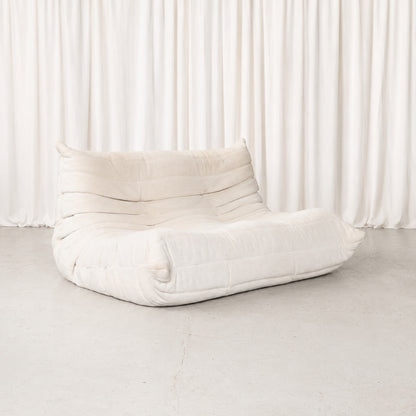 Light Ligne Roset Togo two-seater sofa designed by Michel Ducaroy, upholstered in a soft, neutral fabric with a subtle corduroy-like texture.