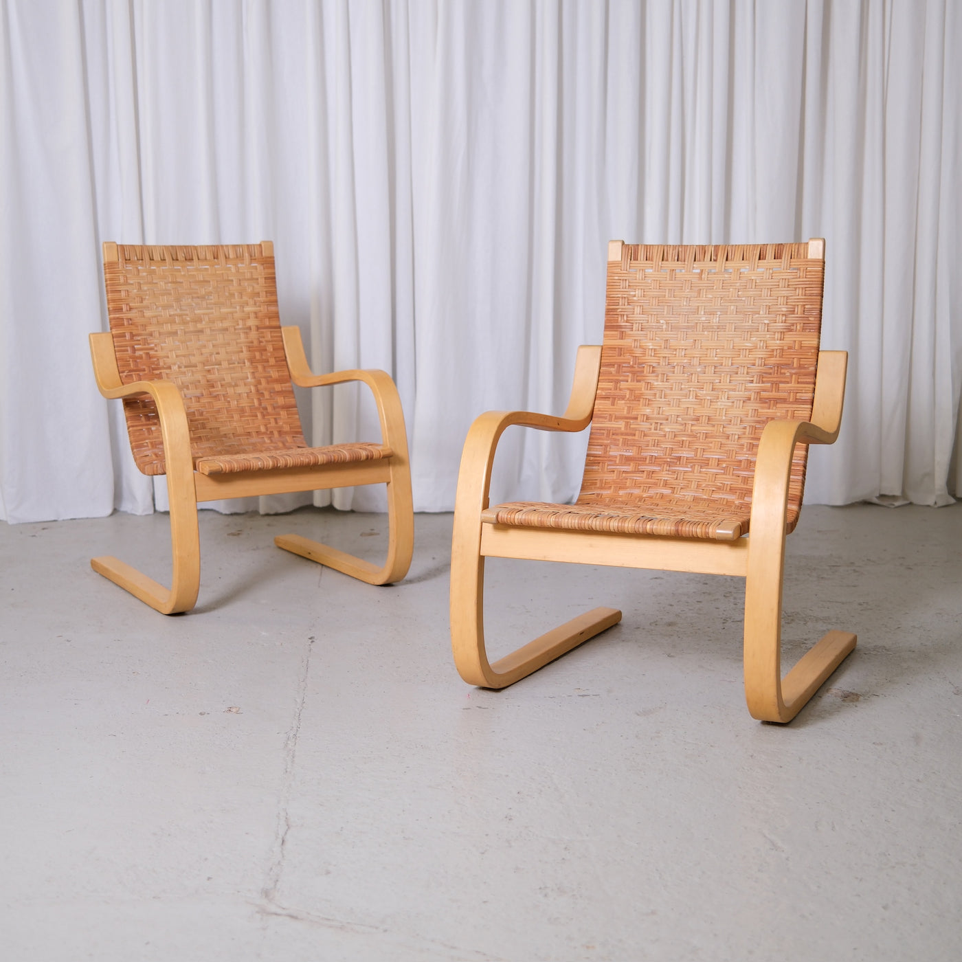 Alvar Aalto 406 lounge chairs for Artek with bent birch frames and woven rattan seats photographed in studio.