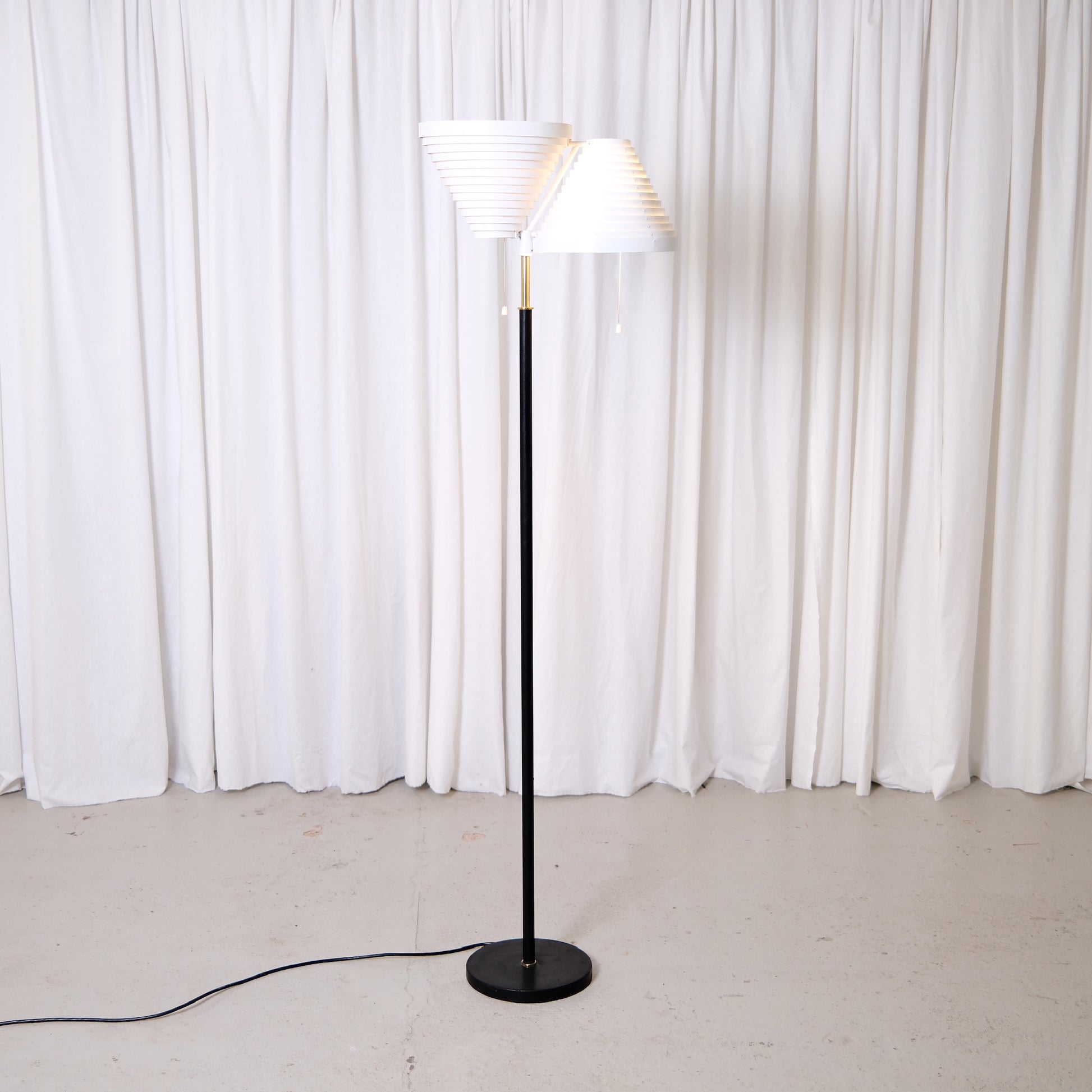 Rare Alvar Aalto A809 floor lamp manufactured by Valaisinpaja. Collectible Finnish modern lighting design with layered white metal shades and brass details.
