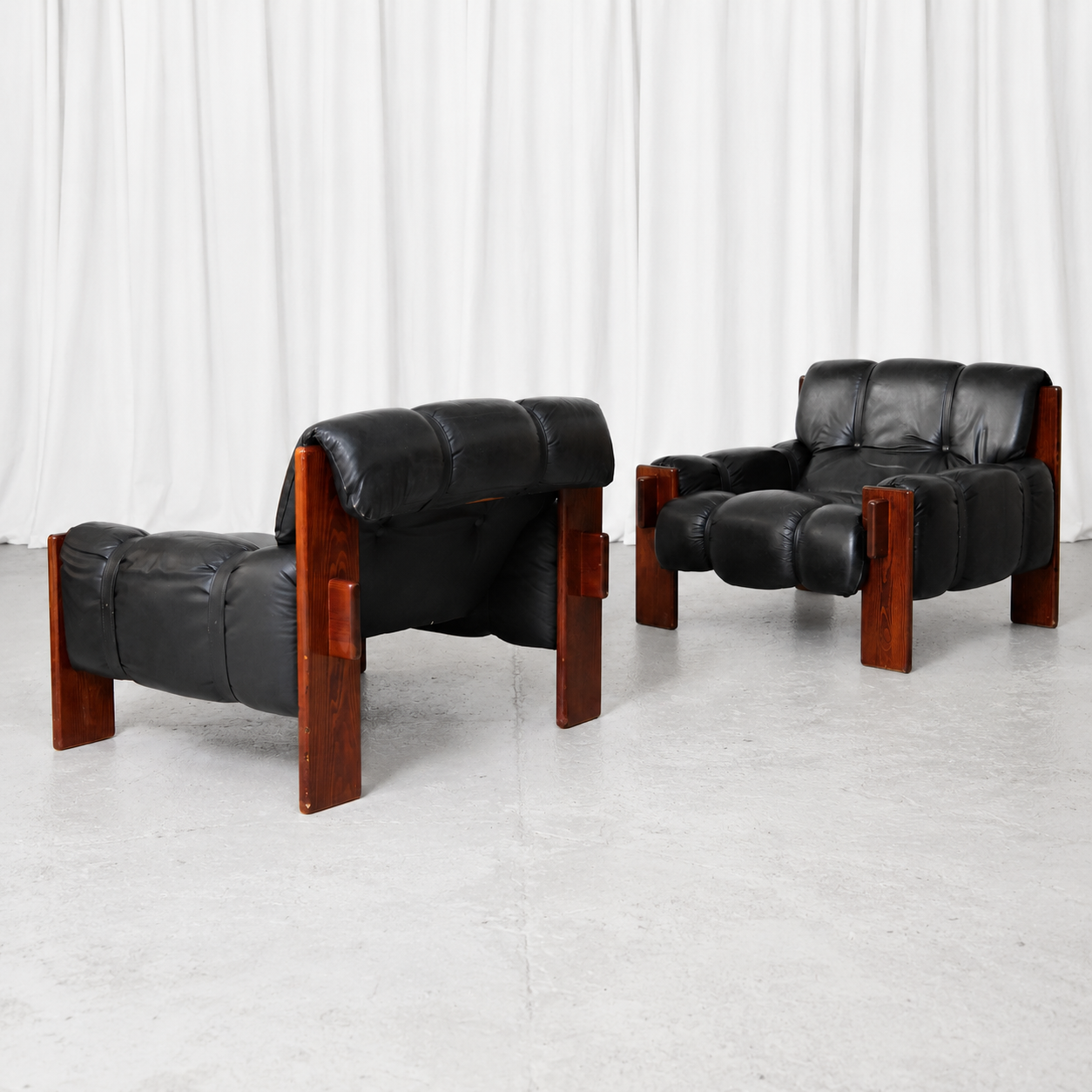 A pair of vintage Brazilian armchairs with black leather upholstery and wooden frames. A bold and comfortable lounge pair with a strong Brazilian modernist character.