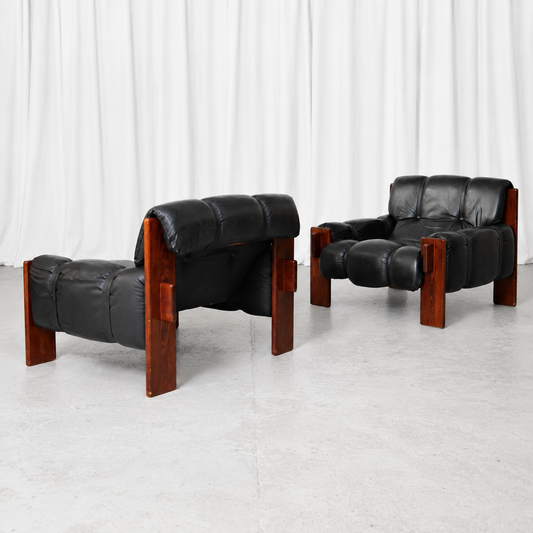 A pair of vintage Brazilian armchairs with black leather upholstery and wooden frames. A bold and comfortable lounge pair with a strong Brazilian modernist character.