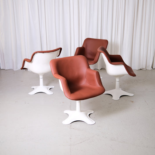 Set of vintage Yrjö Kukkapuro Junior swivel chairs with reddish brown leather upholstery and white bases photographed in studio.