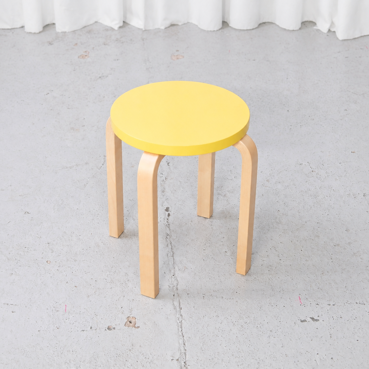 Artek E60 four-legged birch stool with yellow seat, angled view
