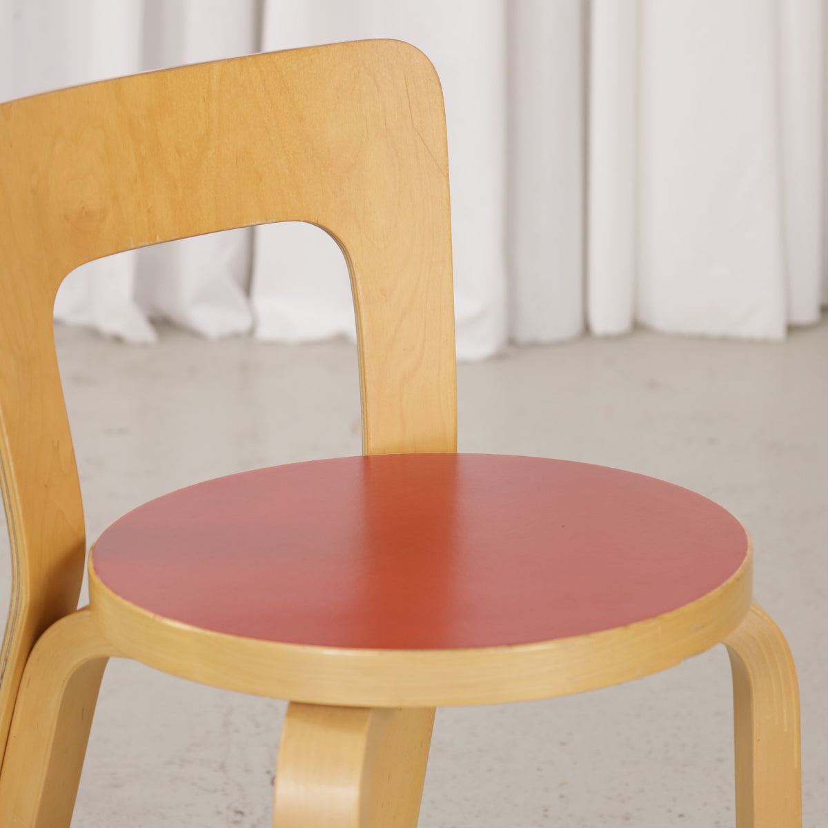 Close-up of red linoleum seat and birch backrest on Artek Chair 65