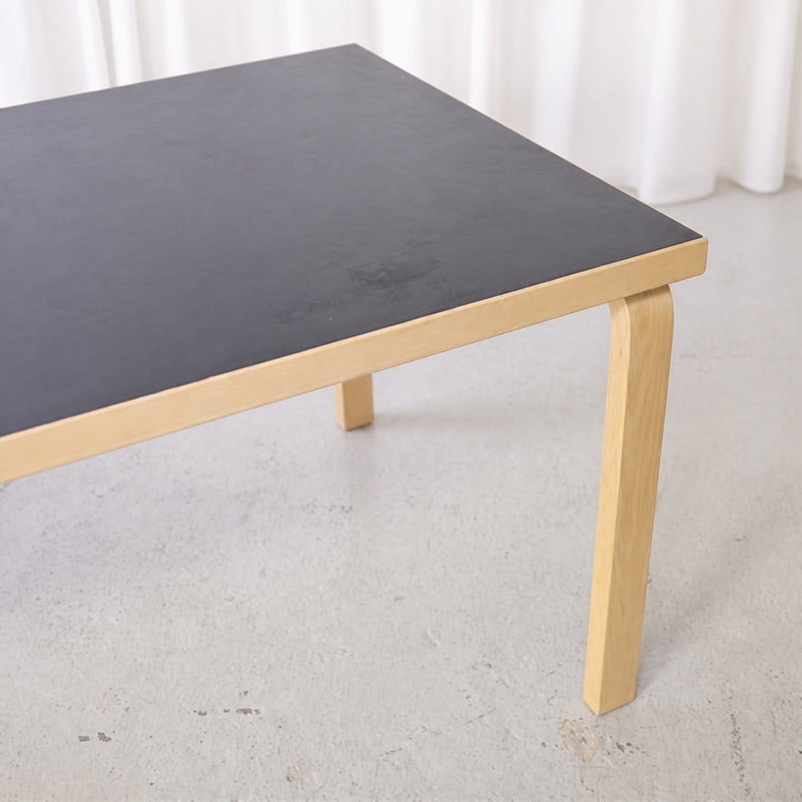 Close view of the black linoleum top and birch L-leg of Artek Table 83