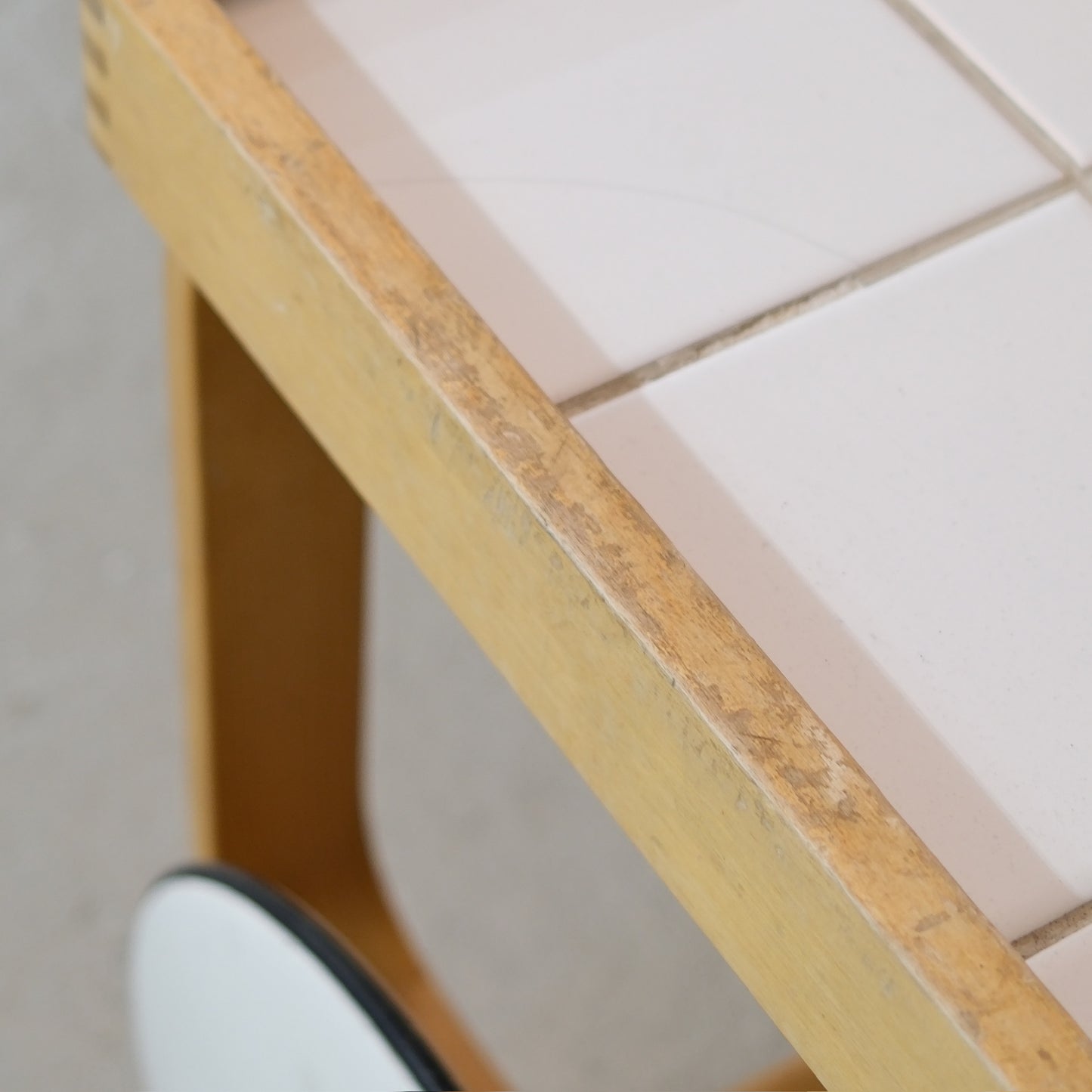 Heavy surface wear on the birch frame beside the tiled top