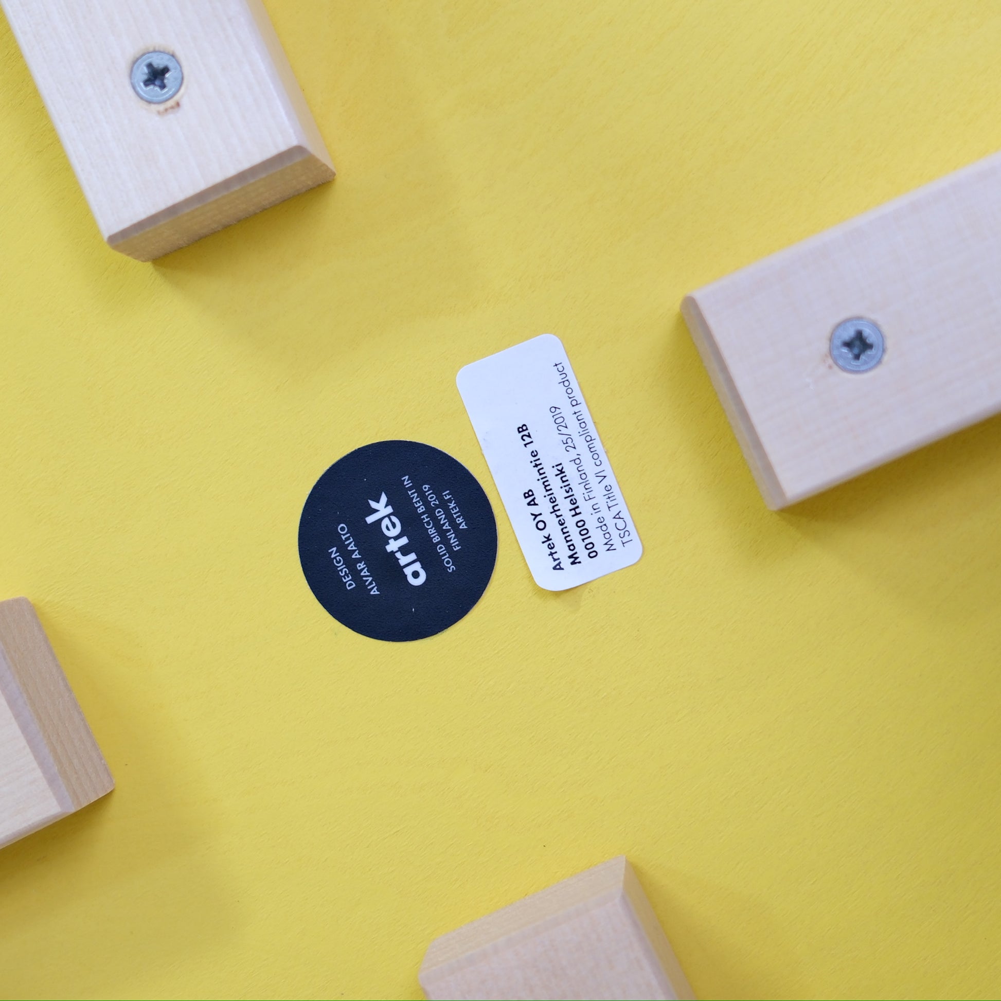 Underside label and four birch leg fixings on the yellow Artek E60 stool