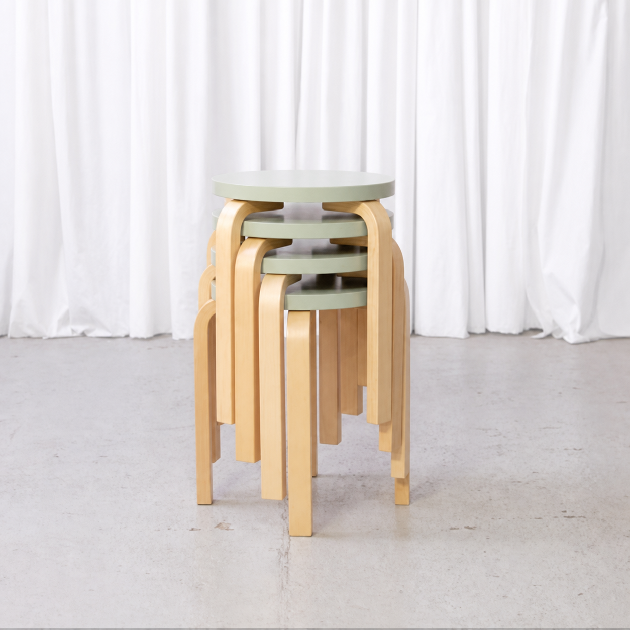 Four Artek E60 stools with mint-green seats stacked in a studio