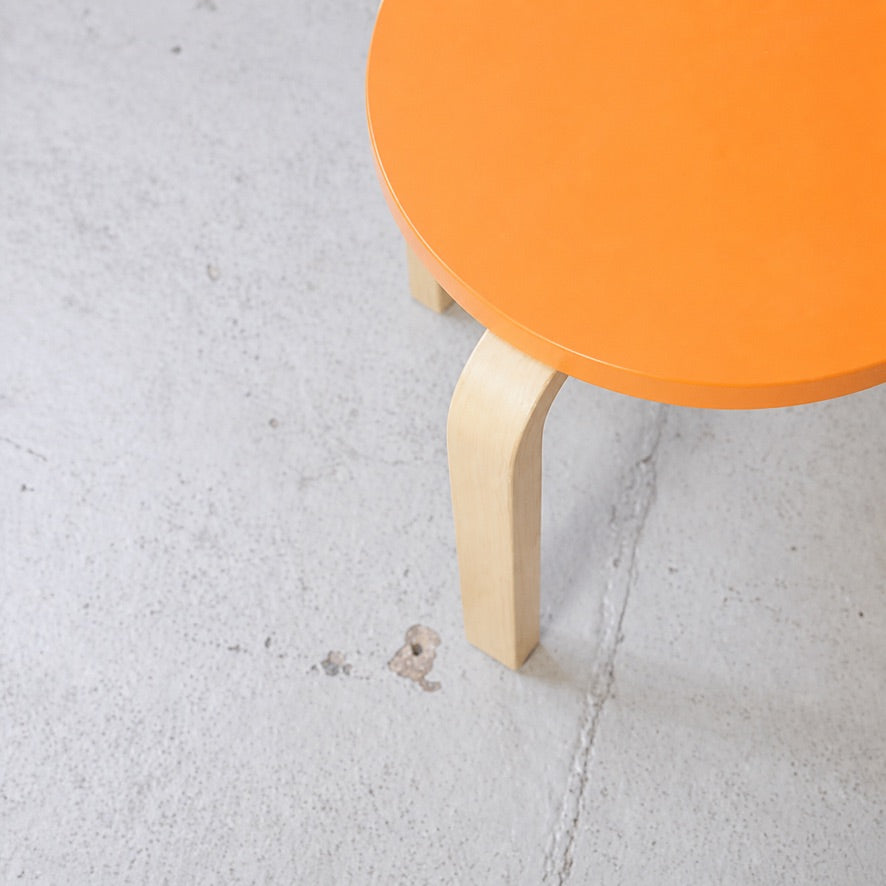Detail of the orange lacquered birch seat and bent birch leg of an Artek E60 stool
