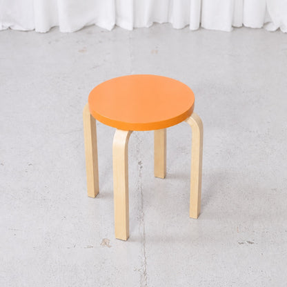 Artek E60 stool viewed from above with an orange lacquered birch seat
