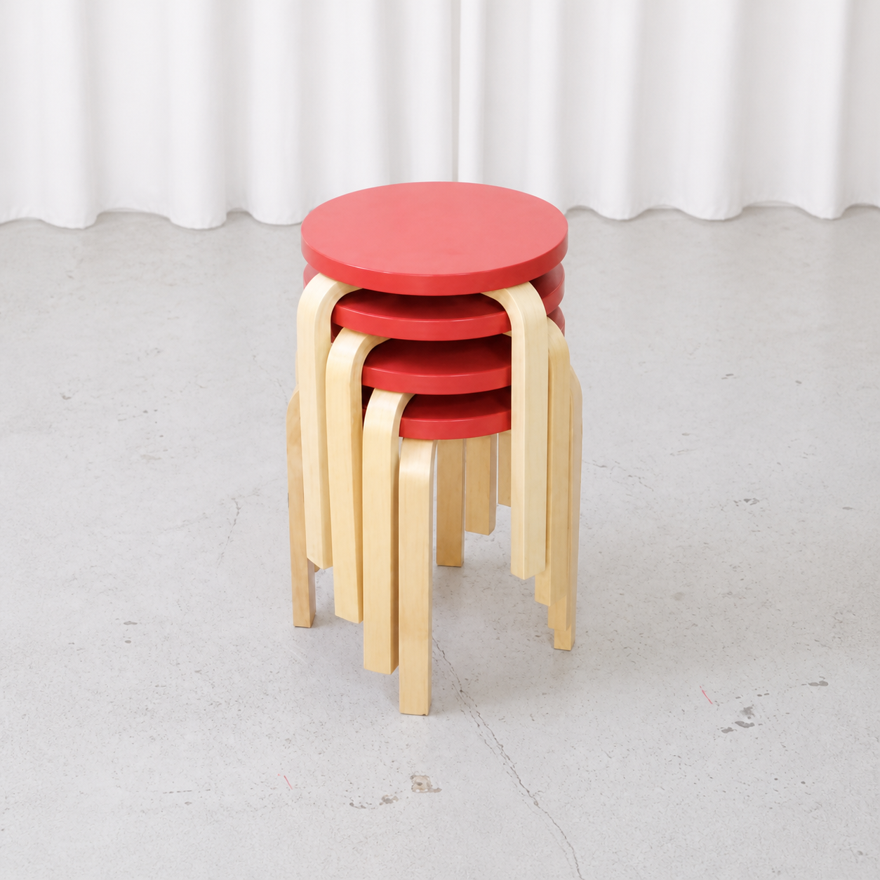Four stackable Artek E60 stools in red lacquered birch, angled view