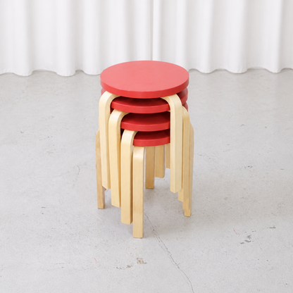 Four stackable Artek E60 stools in red lacquered birch, angled view