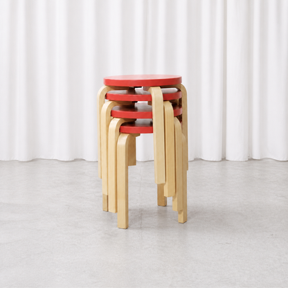 Four Artek E60 stools with red lacquered seats and natural birch legs, stacked