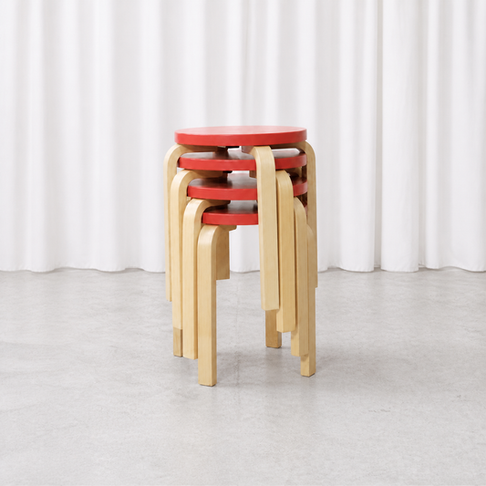 Four Artek E60 stools with red lacquered seats and natural birch legs, stacked