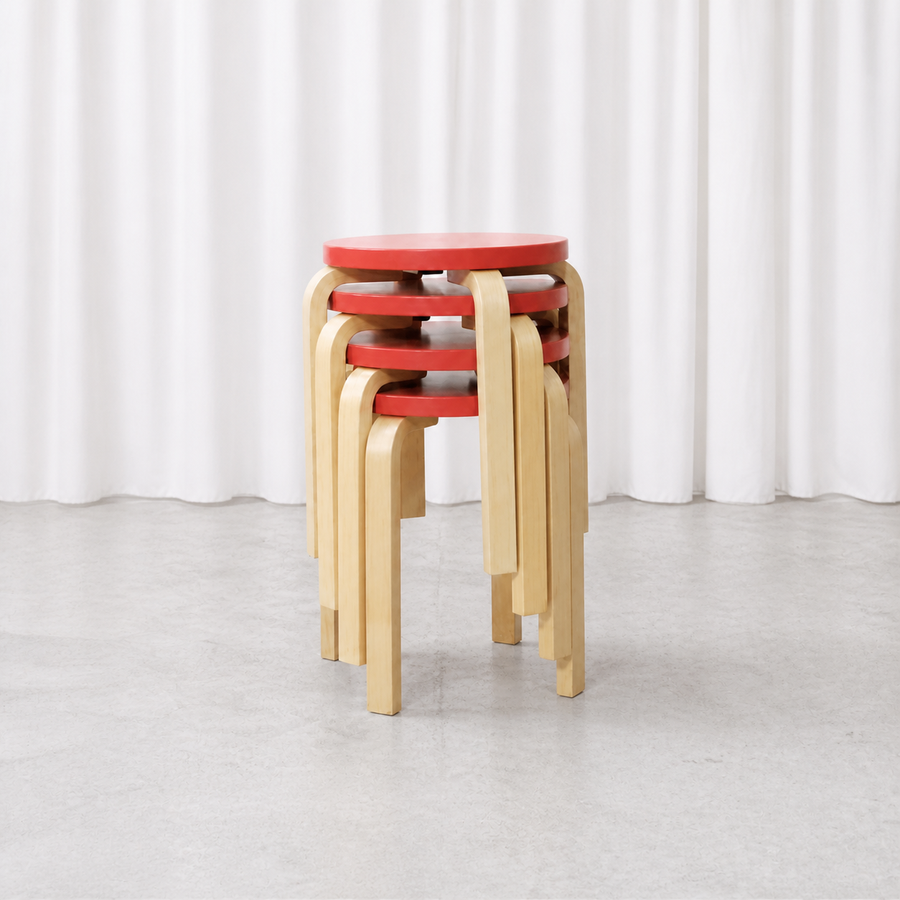 Four Artek E60 stools with red lacquered seats and natural birch legs, stacked