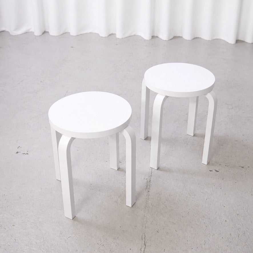 Two white Artek E60 stools shown separately from above
