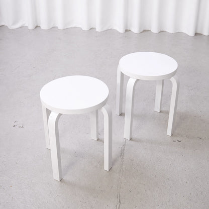 Two white Artek E60 stools shown separately from above