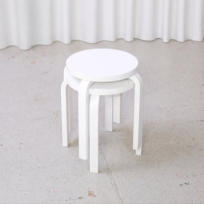 Two white Artek E60 stools stacked in an angled view