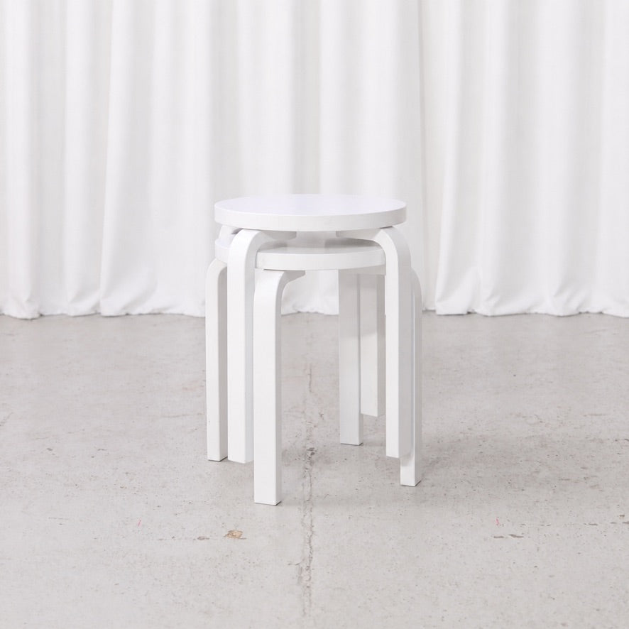 Two white Artek E60 stools by Alvar Aalto stacked in front view