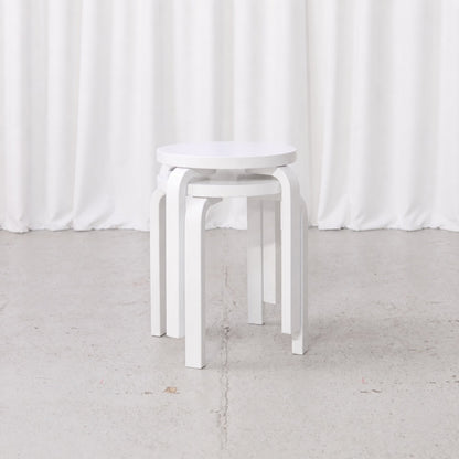Two white Artek E60 stools by Alvar Aalto stacked in front view