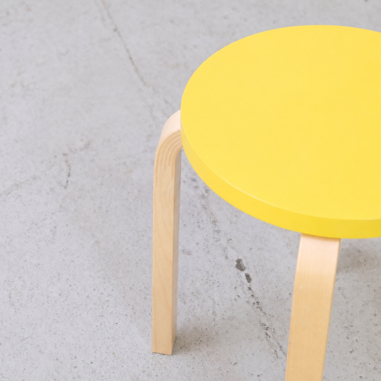 Detail of the yellow lacquered seat and bent birch L-leg on an Artek E60 stool