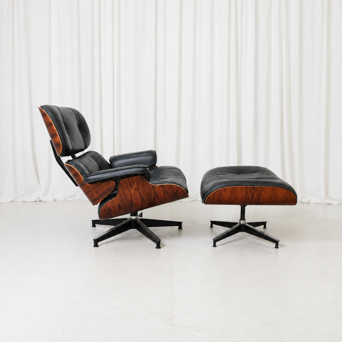 Eames Lounge -nojatuoli ja rahi, joissa on palisanteriviilupinnat ja musta nahkaverhoilu. Kuvattu sivulta.