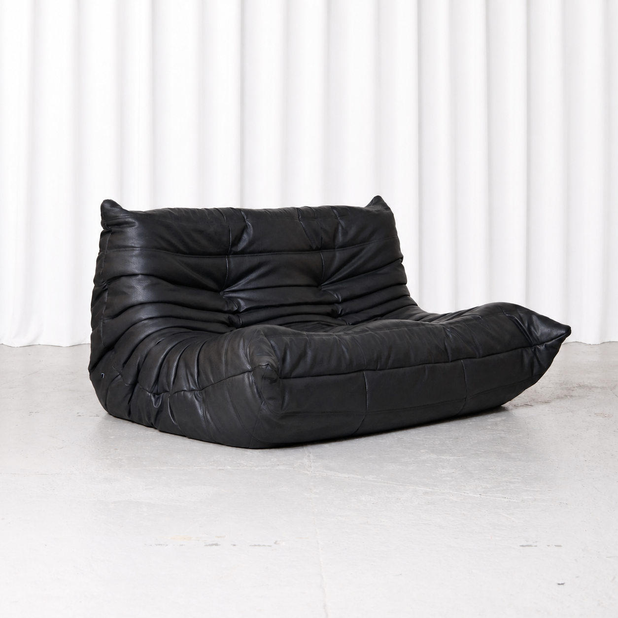 Black synthetic leather Ligne Roset Togo two-seater sofa designed by Michel Ducaroy, front three-quarter view.