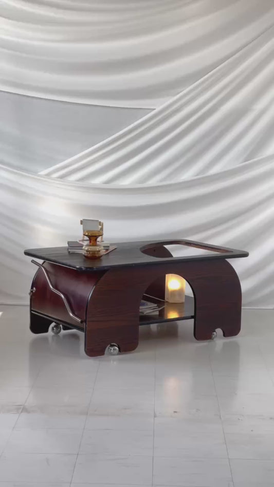 1970s dark-stained oak coffee table with sculptural curves, chrome wheels, and a sliding door storage compartment